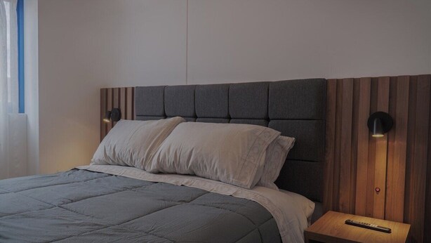 Ein Bett mit grauer Bettdecke, einem Holzkopfende und zwei Nachttischlampen.