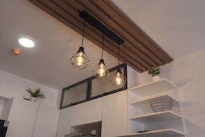 Eine moderne Küche mit Pendelleuchten, weißen Schränken und einem Holzbalken an der Decke.