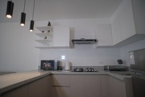 Une cuisine moderne avec des armoires blanches, un four à micro-ondes encastré, une cuisinière à gaz et des luminaires suspendus.