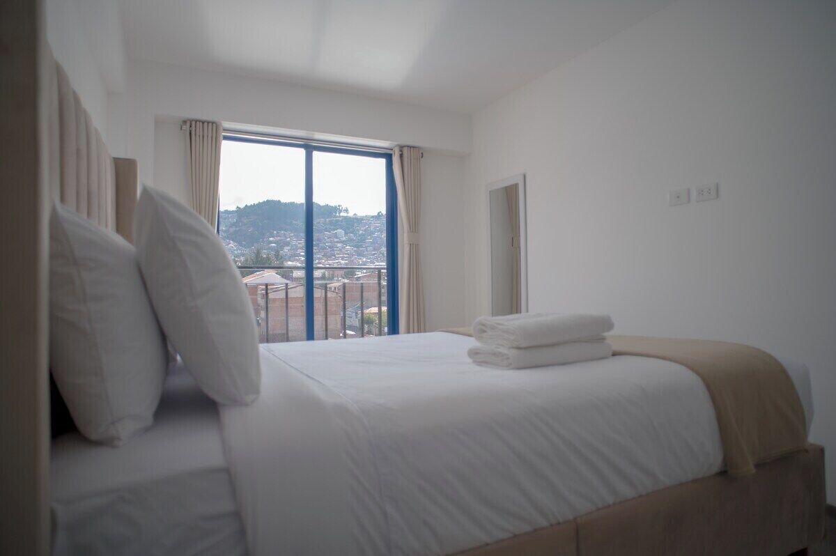 A hotel room with a bed, a window with curtains, and a view of a cityscape.