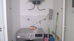 Ein kleiner Hauswirtschaftsraum mit Waschmaschine, Warmwasserbereiter und Reinigungsmitteln.