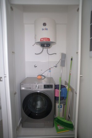 Ein kleiner Hauswirtschaftsraum mit Waschmaschine, Warmwasserbereiter und Reinigungsmitteln.