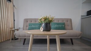 Ein modernes Wohnzimmer mit einem beigefarbenen Sofa, einem runden Holztisch und einer dekorativen Vase mit Blumen.