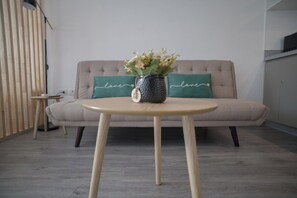 Ein modernes Wohnzimmer mit einem beigefarbenen Sofa, einem runden Holztisch und einer dekorativen Vase mit Blumen.