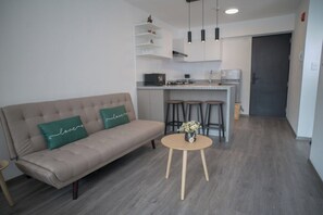 A modern living room with a sofa, a round wooden table with a vase, and a kitchen area with a countertop and stools. - Modern apartment with 2 sleeping areas (Cusco)