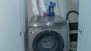 Ein kleiner Waschraum mit einer Waschmaschine mit Frontlader, einem Wäscheständer und einem Warmwasserbereiter.