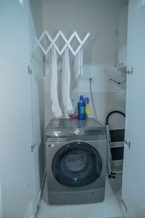 Ein kleiner Waschraum mit einer Waschmaschine mit Frontlader, einem Wäscheständer und einem Warmwasserbereiter.