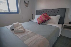 A neatly made bed with a grey headboard, white pillows, and a folded white towel on the bed. - Modern studio near Qorikancha (Cusco)