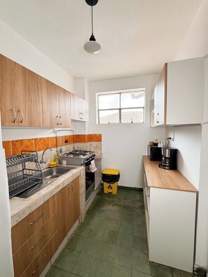 A compact kitchen with wooden cabinets, a sink, a stove, and a window. - Spacious vintage apartment in Zarumilla (Cusco)