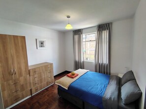 A bedroom with a bed, a wardrobe, a bedside table, and a window with curtains. - Spacious vintage apartment in Zarumilla (Cusco)
