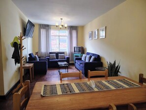A living room with a dining table, sofas, a TV, and a coat rack. - Spacious vintage apartment in Zarumilla (Cusco)