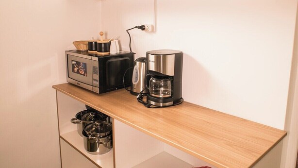Ett litet, praktiskt kök med en kaffebryggare, en brödrost och en mikrovågsugn placerade på en bänkskiva i trä.