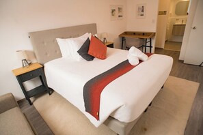 A neatly made bed with a headboard, a bedside table with a lamp, and a small desk with a chair. - Spacious family apartment near the center (Cusco)