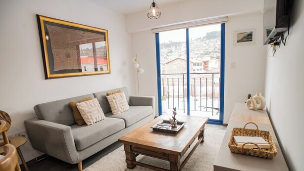 Ein Wohnzimmer mit Sofa, Couchtisch und Blick auf eine Stadtlandschaft durch einen Balkon.