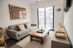 Ein Wohnzimmer mit Sofa, Couchtisch und Blick auf eine Stadtlandschaft durch einen Balkon.