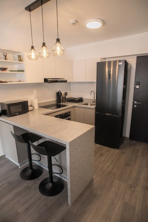 A modern kitchen with a central island, black appliances, and pendant lighting. - Spacious family apartment near the center (Cusco)