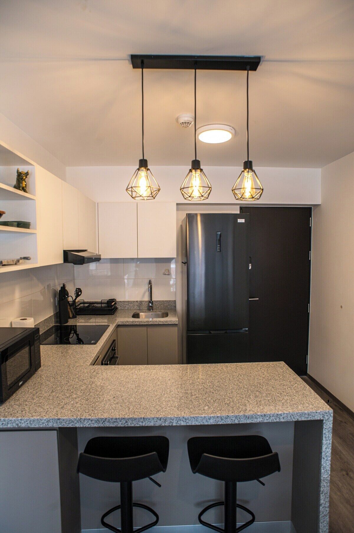 A modern kitchen with a central island, stainless steel appliances, pendant lighting, and a black refrigerator.