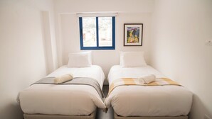 Ein Doppelzimmer mit zwei Betten, einem Fenster mit blauen Rahmen und einem Bild an der Wand.