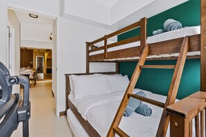 A bunk bed with a wooden frame and white bedding, a green accent wall, and a visible bathroom in the background. - Oak & Sage | 2BR | King Bed | IT Park | Fast Wi-Fi (Cebu City)