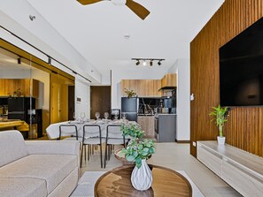 A modern living room with a dining area, kitchen, and a large TV. - Oak & Sage | 2BR | King Bed | IT Park | Fast Wi-Fi (Cebu City)