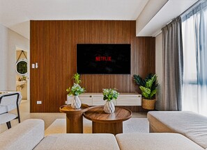 A modern living room with a flat-screen TV mounted on a wooden wall, two side tables with vases, and a sofa. - Oak & Sage | 2BR | King Bed | IT Park | Fast Wi-Fi (Cebu City)