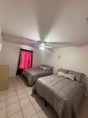 A bedroom with two beds, a ceiling fan, a window with red curtains, and a tiled floor. - 2-bedroom apartment in welcoming Harlingen with AC comfort (Harlingen)