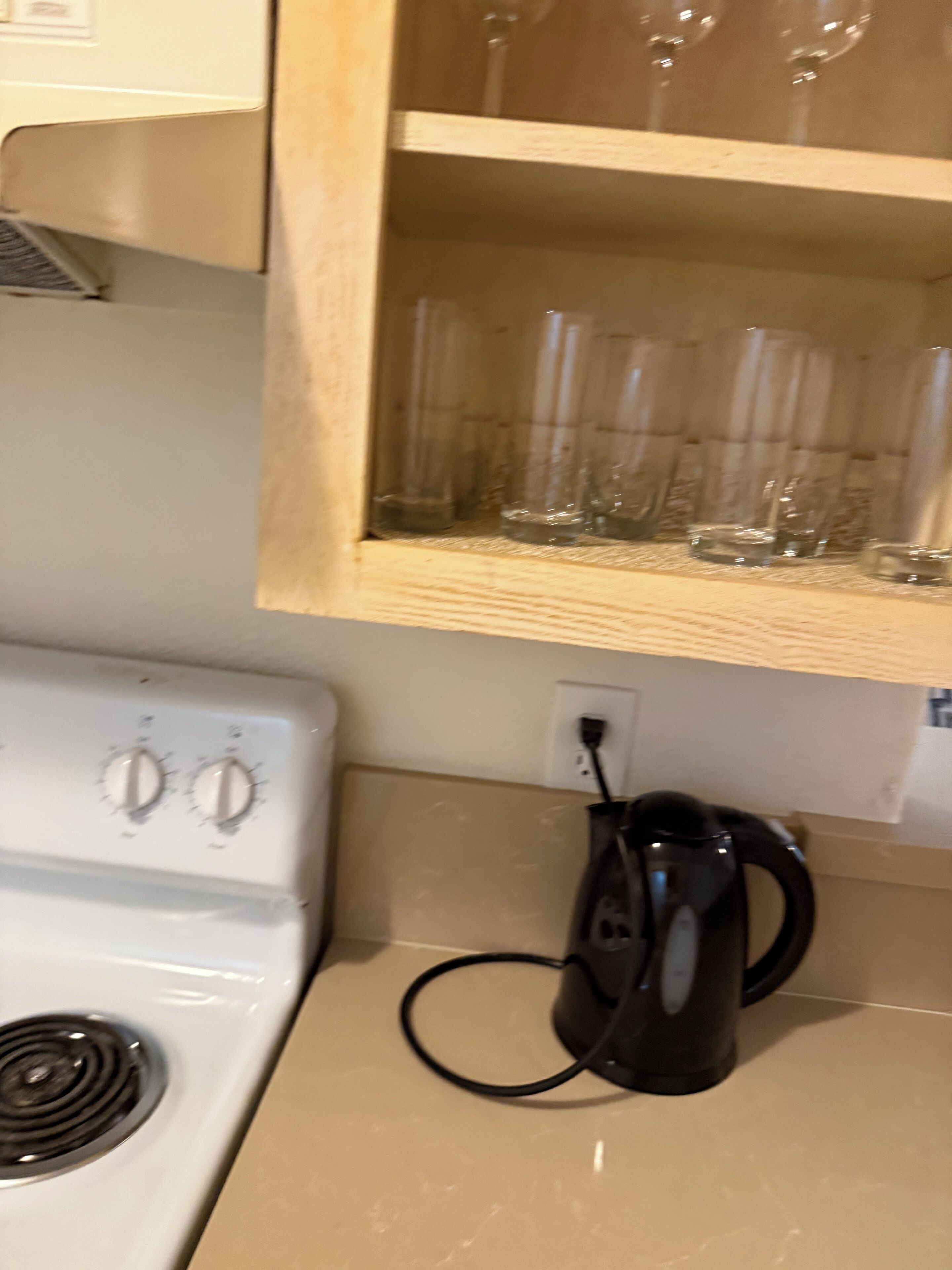 Une cuisine équipée d’une cuisinière, d’une bouilloire et d’une étagère où sont rangés des verres transparents.