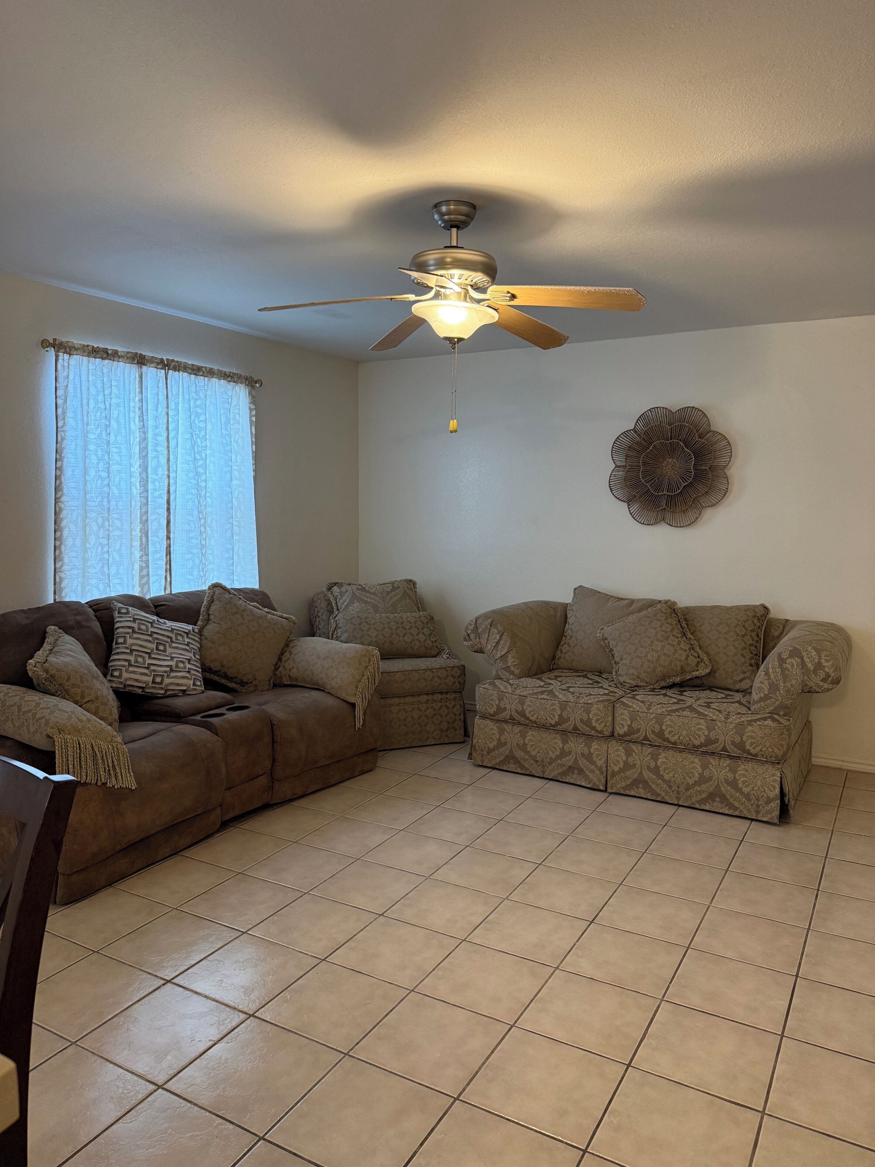 A living room with a sectional sofa, a ceiling fan, and a decorative wall piece.