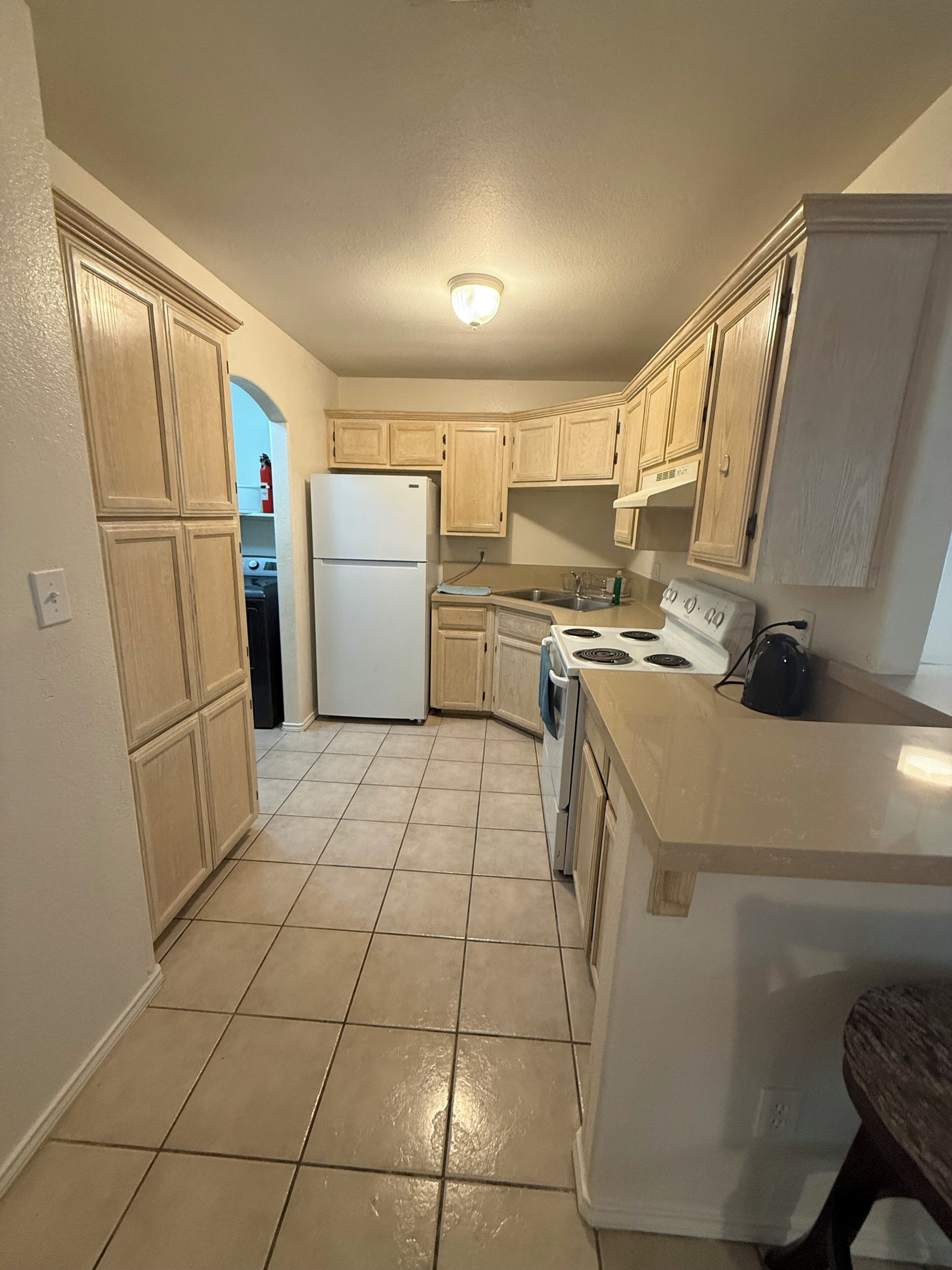 A kitchen with light wooden cabinets, a white refrigerator, a stove, and a sink.