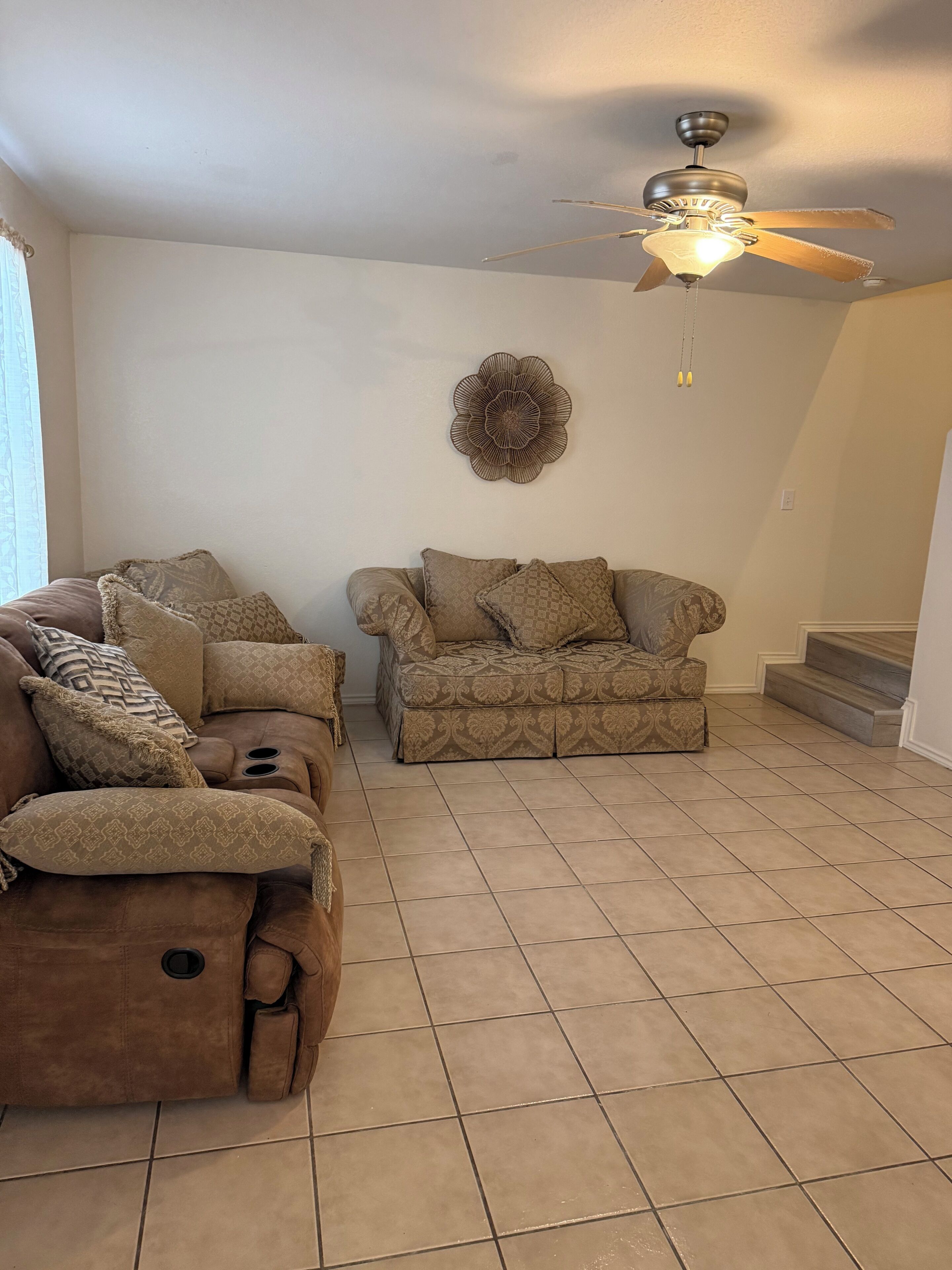 A living room with a sofa, a recliner, a ceiling fan, and a decorative wall piece.