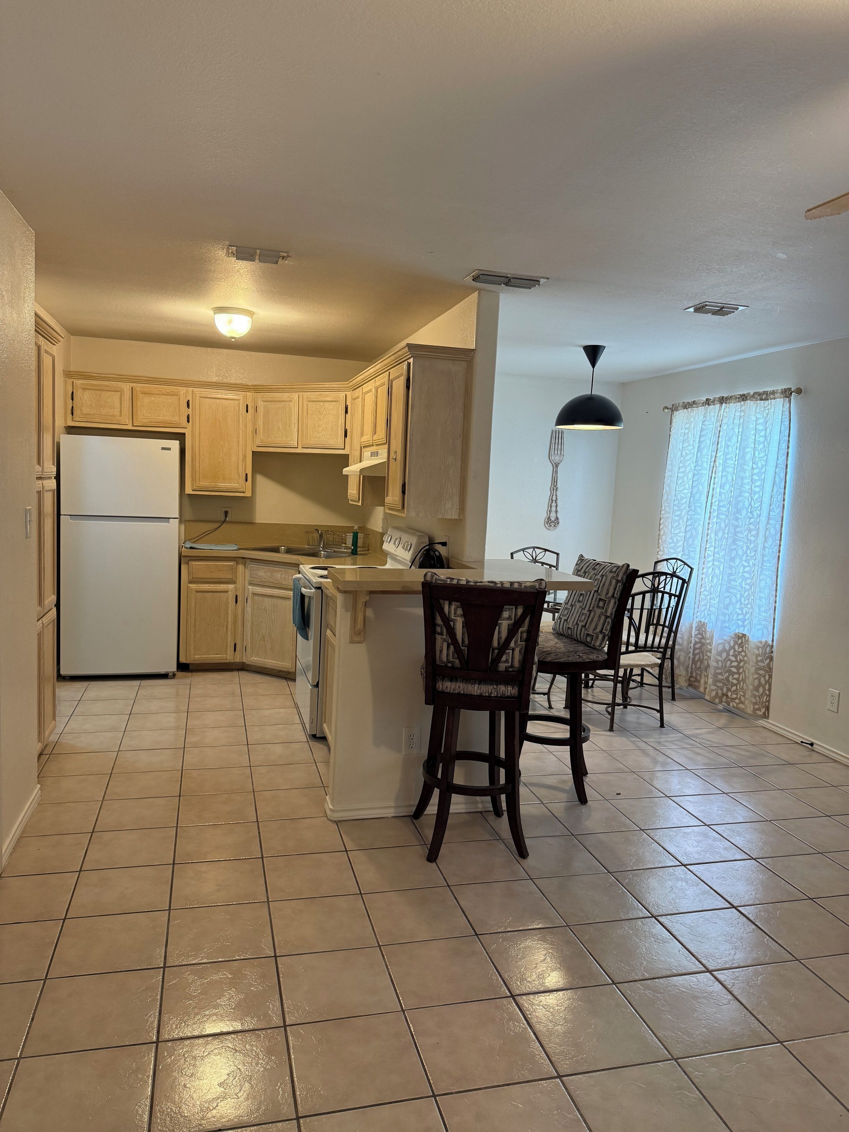 A kitchen with a refrigerator, wooden cabinets, a sink, and a dining area with chairs and a table.