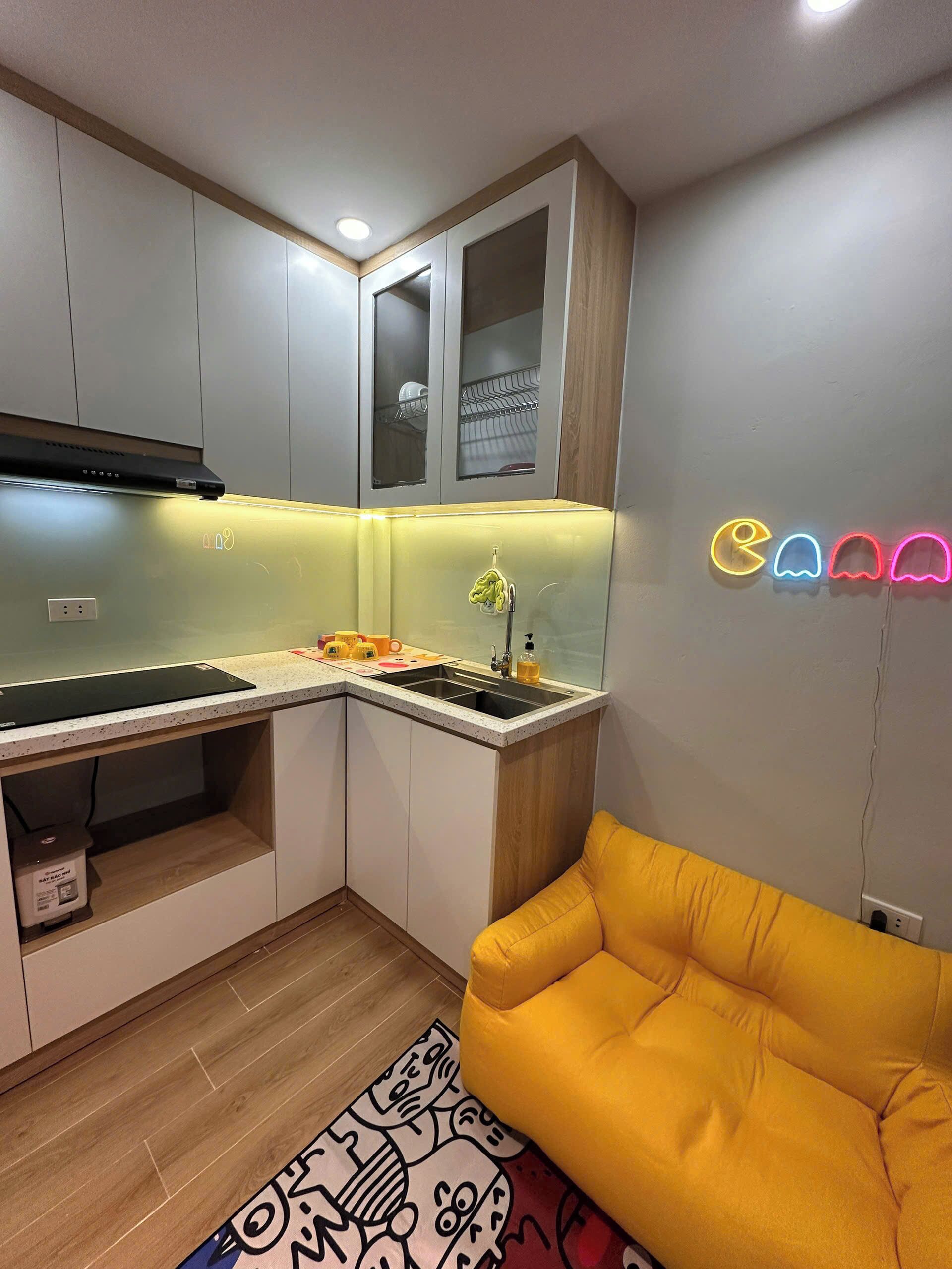 A compact kitchen with a built-in stove, a sink, and a small countertop. There is a yellow sofa in the adjacent living area.