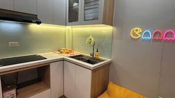 A compact kitchen with a built-in stove, a sink, and a small countertop. There is a yellow sofa in the adjacent living area.