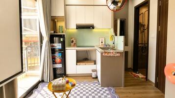 A compact kitchen with a refrigerator, microwave, and sink. There's a small dining area with a checkered rug and a yellow table.