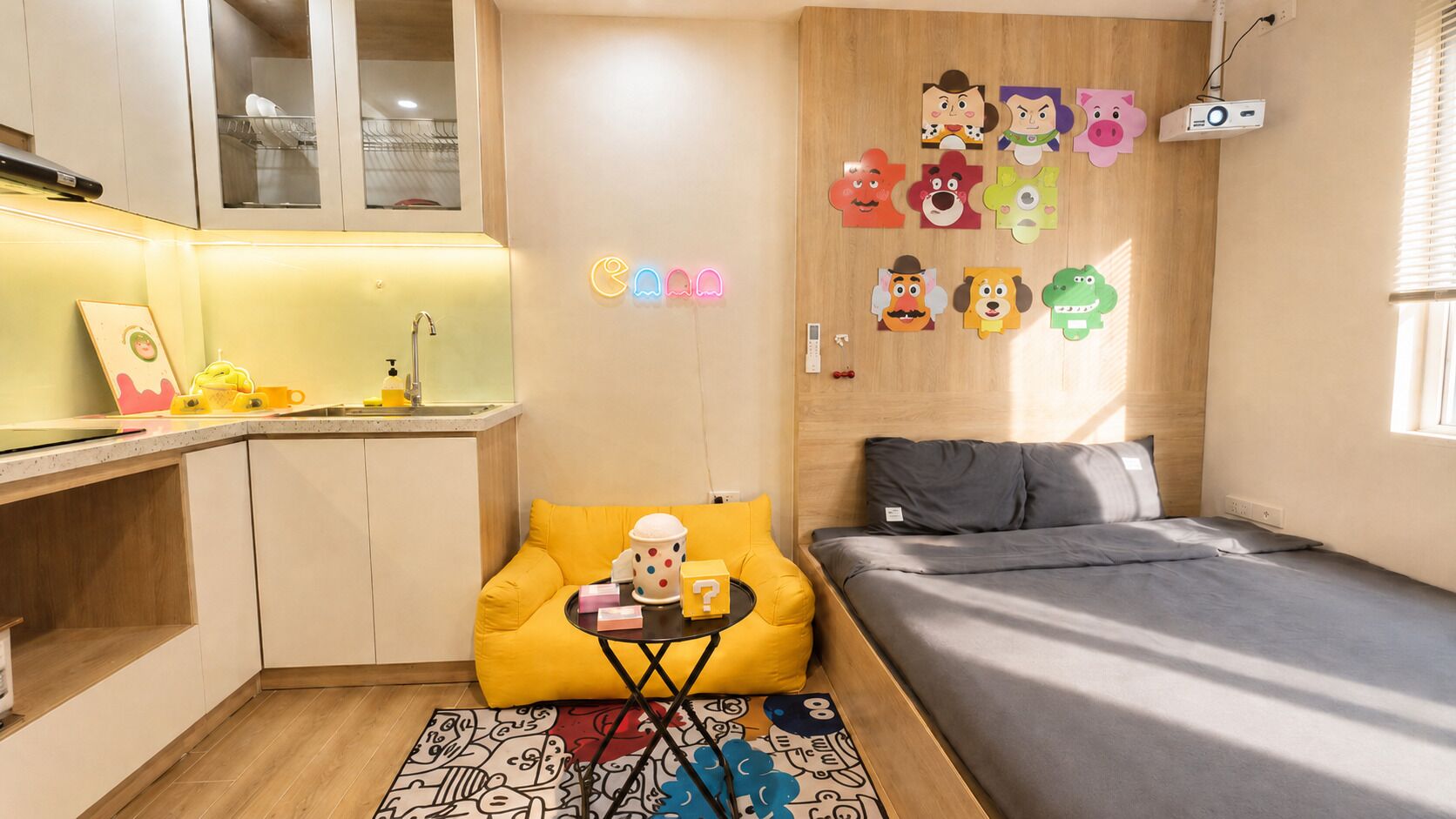 Une pièce compacte comprenant un coin cuisine, un lit, une petite table avec une tasse à pois et une décoration murale colorée.