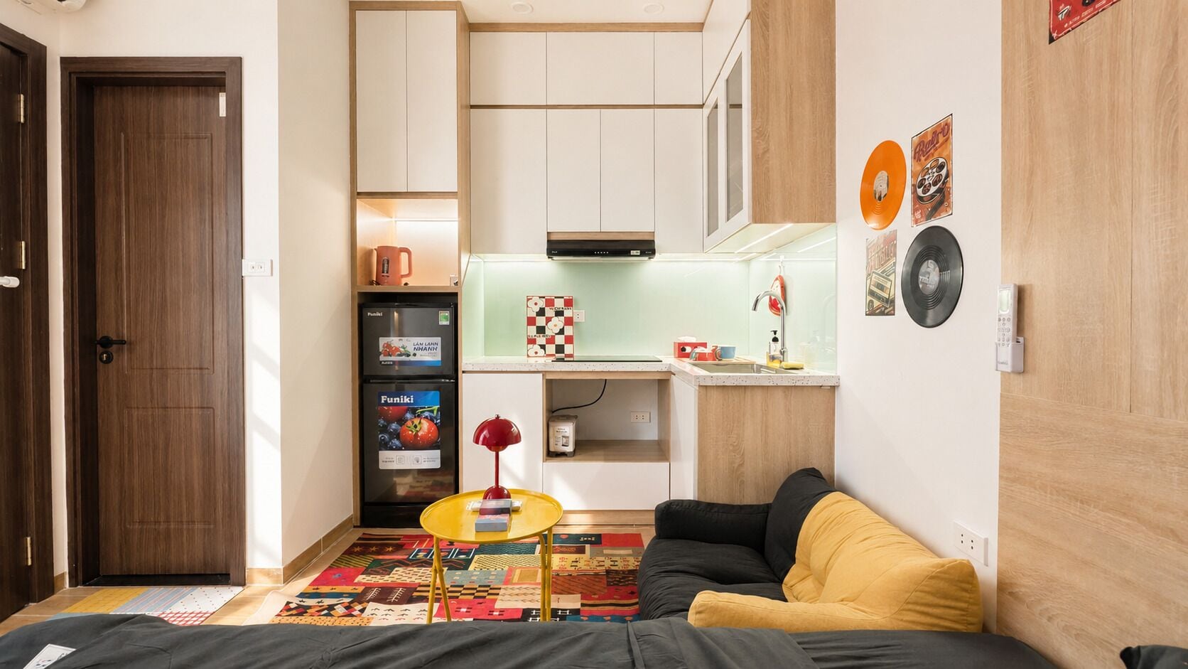 A compact living space with a kitchenette, a sofa, a small table, and a patterned rug.