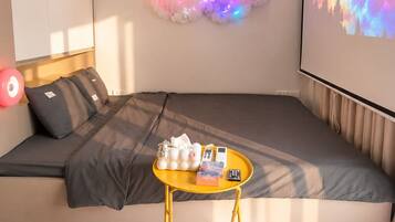 A cozy room with a sofa, a small table, a projector screen, and a cloud-shaped light installation.