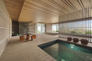 A modern indoor pool area with a wooden floor, a seating area with benches, and a view through a wooden partition.