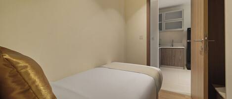 A bedroom with a bed, a door leading to a bathroom, and a wooden wardrobe.