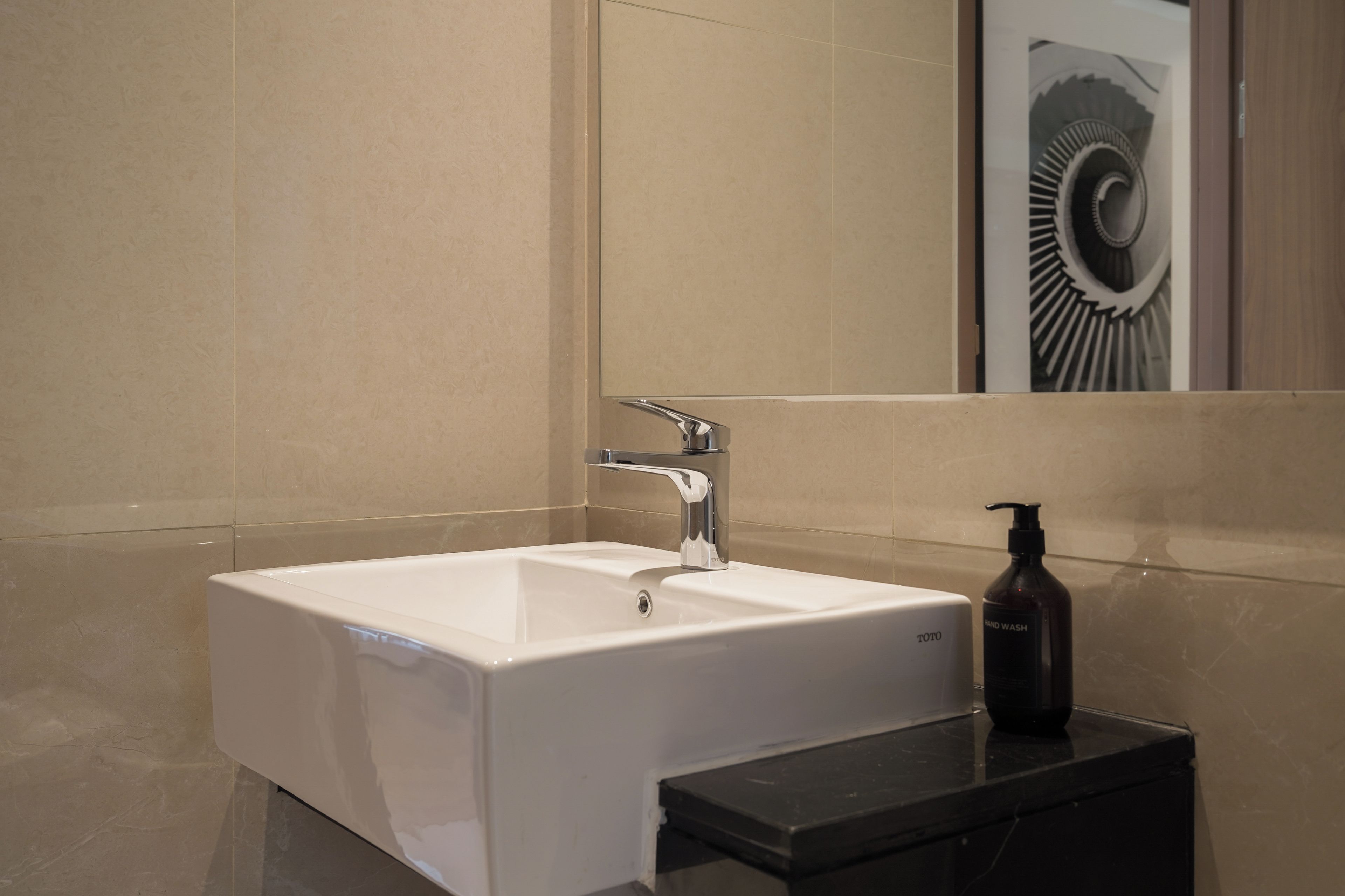 A bathroom with a white sink, a mirror, and a black soap dispenser.