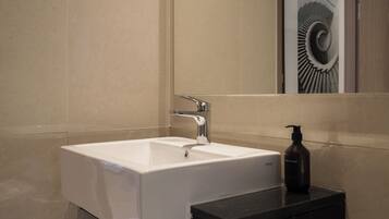 A bathroom with a white sink, a mirror, and a black soap dispenser.