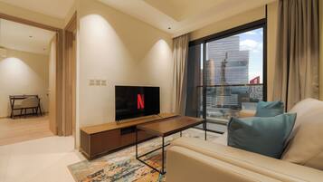 A modern living room with a flat-screen TV, a sofa, a coffee table, and a view of a cityscape through a large window.