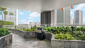 An outdoor patio area with a grill, surrounded by planters and overlooking a cityscape.