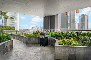 An outdoor patio area with a grill, surrounded by planters and overlooking a cityscape.