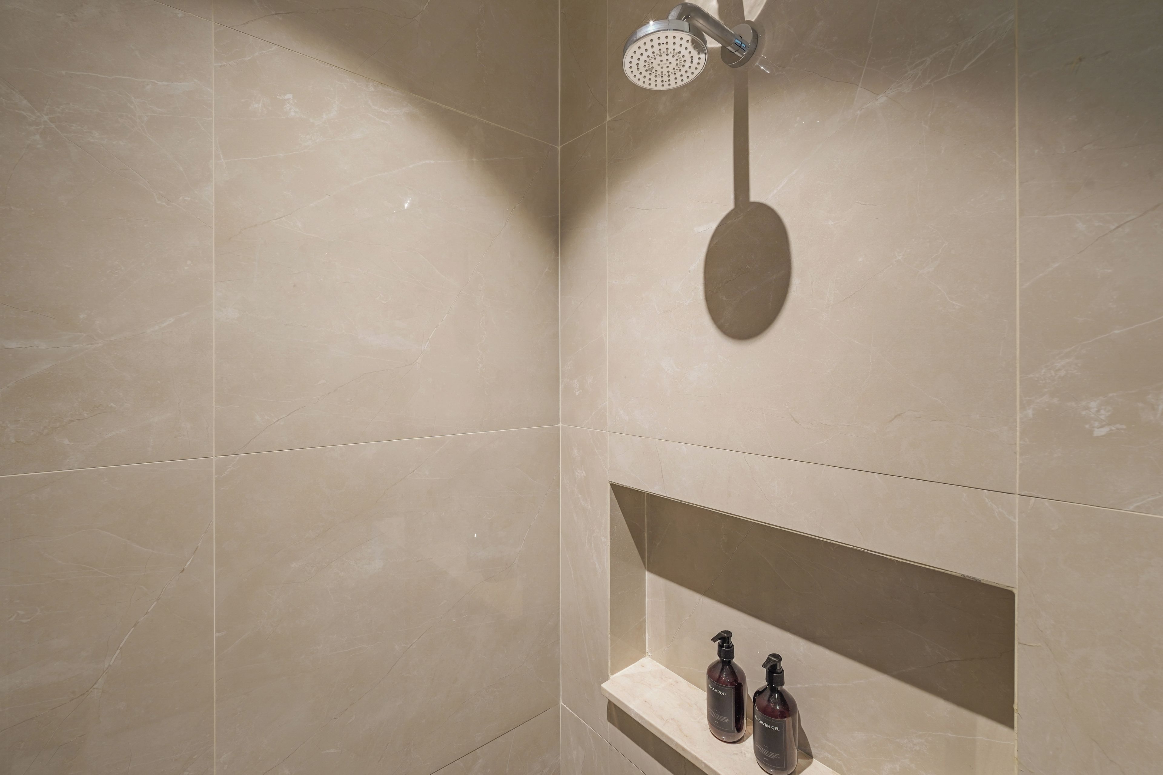 A bathroom with a shower, a vanity with a shelf, and two bottles of shampoo and shower gel.