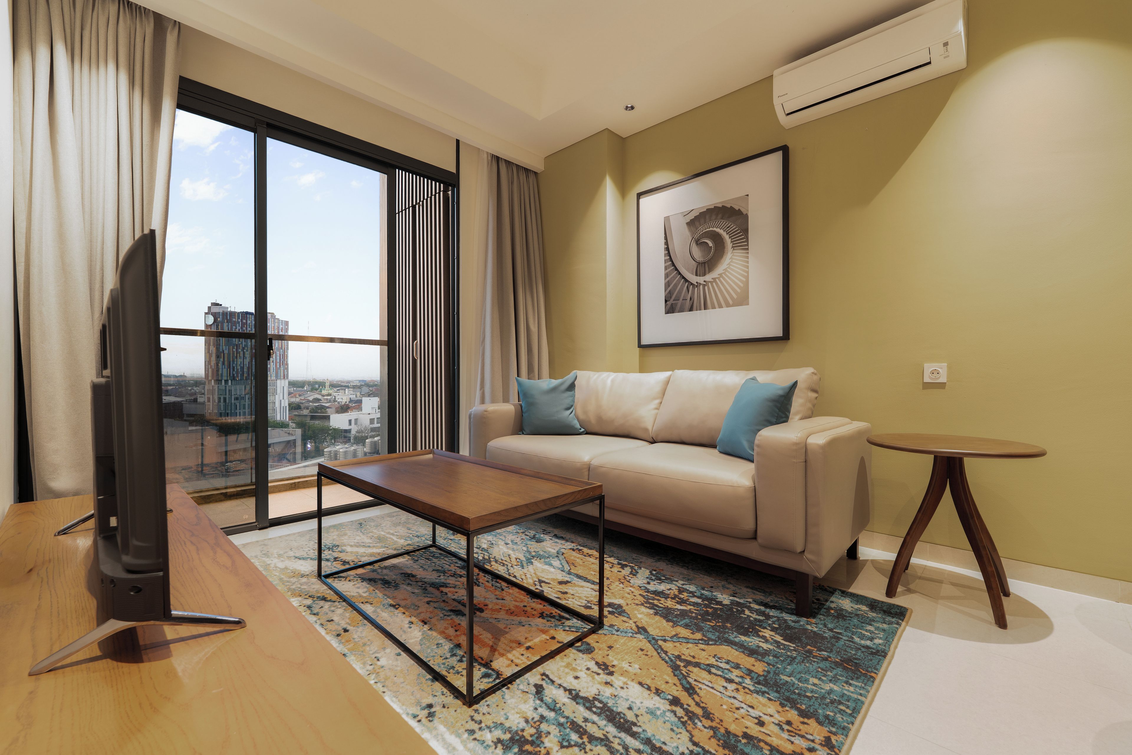 Un moderno salón con sofá, mesa de centro y vistas de la ciudad a través de grandes ventanales.