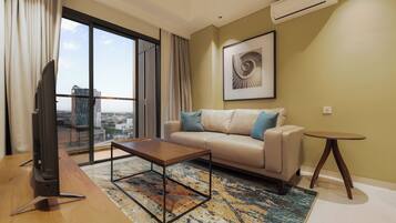 Un moderno salón con sofá, mesa de centro y vistas de la ciudad a través de grandes ventanales.