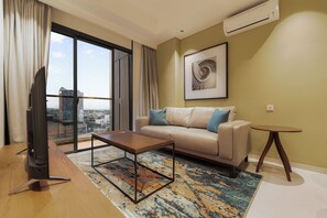 Uma sala de estar moderna com sofá, mesa de centro e vista para a cidade através de grandes janelas.