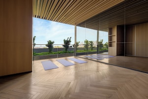 A spacious room with a large window, wooden flooring, and exercise mats.