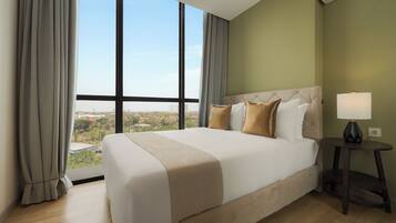 A hotel room with a large bed, a nightstand, a lamp, and a view of a cityscape through large windows.